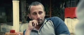 Movie still from “Rust and Bone” (2012), directed by Jacques Audiard – A person sitting down with his hand under his chin; Close Up shot, Low angle