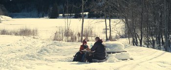 Movie still from “Rust and Bone” (2012), directed by Jacques Audiard – A man and a woman sitting in the middle of a snowy field; Extreme Wide shot, High angle