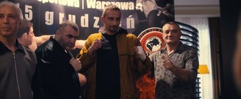 Movie still from “Rust and Bone” (2012), directed by Jacques Audiard – A man in a brown jacket holding a black shirt; Medium shot, High angle