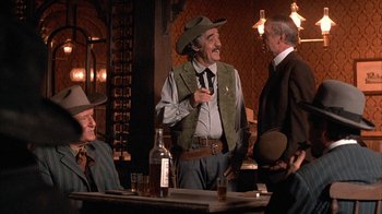 Movie still from “Rustlers' Rhapsody” (1985), directed by Hugh Wilson – A group of men sitting at a table in a room; Medium shot, Over the shoulder angle
