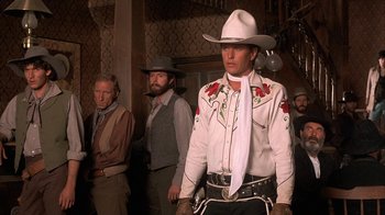 Movie still from “Rustlers' Rhapsody” (1985), directed by Hugh Wilson – A man in a white cowboy hat standing in front of other men; Medium shot, Low angle