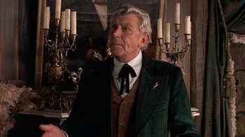 Movie still from “Rustlers' Rhapsody” (1985), directed by Hugh Wilson – An older man wearing a suit and tie in front of a painting; Medium shot, Over the shoulder angle