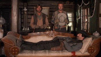 Movie still from “Rustlers' Rhapsody” (1985), directed by Hugh Wilson – Two men standing in front of a bed in a log cabin; Wide shot, Low angle