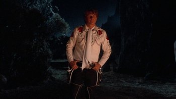 Movie still from “Rustlers' Rhapsody” (1985), directed by Hugh Wilson – A man in a white shirt is standing in the dark; Medium shot, Low angle