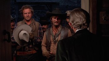 Movie still from “Rustlers' Rhapsody” (1985), directed by Hugh Wilson – A group of men standing next to each other in a room; Medium shot, Over the shoulder angle