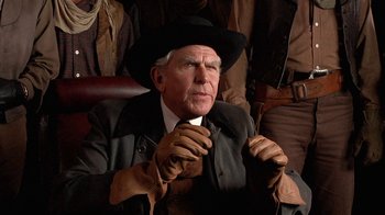 Movie still from “Rustlers' Rhapsody” (1985), directed by Hugh Wilson – An older man wearing a hat and leather gloves; Close Up shot, Over the shoulder angle