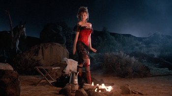 Movie still from “Rustlers' Rhapsody” (1985), directed by Hugh Wilson – A woman standing next to a fire in the desert; Wide shot, Low angle