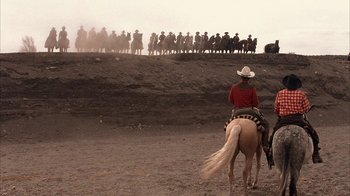 Movie still from “Rustlers' Rhapsody” (1985), directed by Hugh Wilson – A man riding a horse in front of a group of people; Extreme Wide shot, Over the shoulder angle