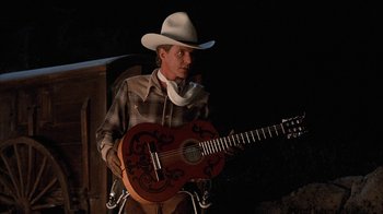Movie still from “Rustlers' Rhapsody” (1985), directed by Hugh Wilson – A man in a cowboy hat is holding a guitar; Medium shot, Low angle