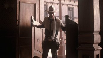 Movie still from “Rustlers' Rhapsody” (1985), directed by Hugh Wilson – A man in a cowboy hat standing in front of an open door; Wide shot, Low angle