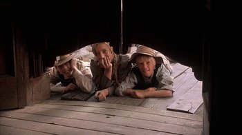 Movie still from “Rustlers' Rhapsody” (1985), directed by Hugh Wilson – Three young boys laying on the ground under an umbrella; Medium shot, Low angle