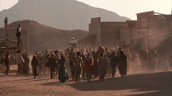 Movie still from “Rustlers' Rhapsody” (1985), directed by Hugh Wilson – A group of people are walking in the dirt; Extreme Wide shot, Low angle