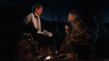 Movie still from “Rustlers' Rhapsody” (1985), directed by Hugh Wilson – Two men sitting next to each other near a fire pit; Medium shot, Low angle