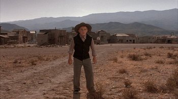 Movie still from “Rustlers' Rhapsody” (1985), directed by Hugh Wilson – A boy in a hat stands in the middle of an empty field; Wide shot, Low angle