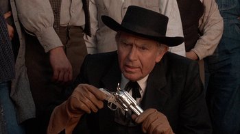 Movie still from “Rustlers' Rhapsody” (1985), directed by Hugh Wilson – An older man in a suit and hat holding a gun; Close Up shot, Over the shoulder angle