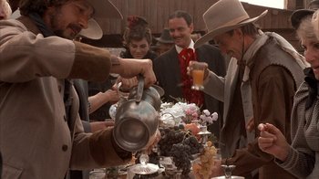 Movie still from “Rustlers' Rhapsody” (1985), directed by Hugh Wilson – A group of people standing around a table with food; Medium shot, Low angle