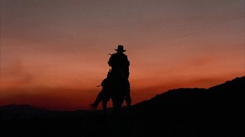 Movie still from “Rustlers' Rhapsody” (1985), directed by Hugh Wilson – A man riding a horse at sunset with the sky in the background; Wide shot, Low angle
