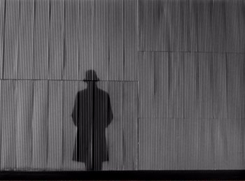 Movie still from “Saboteur” (1942), directed by Alfred Hitchcock – A man standing in front of a wall with his shadow on it; Wide shot, Low angle