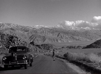 Movie still from “Saboteur” (1942), directed by Alfred Hitchcock – A man riding a bike down the middle of a road; Extreme Wide shot, High angle