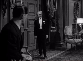 Movie still from “Saboteur” (1942), directed by Alfred Hitchcock – An older man in a tuxedo standing in front of another man in a suit; Medium shot, Over the shoulder angle