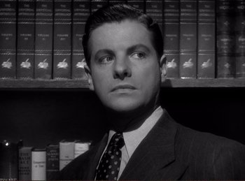 Movie still from “Saboteur” (1942), directed by Alfred Hitchcock – A man in a suit and tie in front of a book shelf; Close Up shot, Low angle