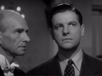 Movie still from “Saboteur” (1942), directed by Alfred Hitchcock – A man in a suit and tie standing next to another man in a suit and tie; Close Up shot, Low angle