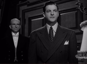 Movie still from “Saboteur” (1942), directed by Alfred Hitchcock – A man in a suit and tie standing next to another man in a suit and tie; Medium shot, Low angle