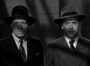 Movie still from “Saboteur” (1942), directed by Alfred Hitchcock – A couple of men in suits and hats standing next to each other; Close Up shot, Low angle