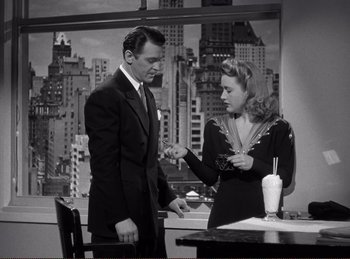 Movie still from “Saboteur” (1942), directed by Alfred Hitchcock – A man and a woman are standing in front of a table; Medium shot, High angle