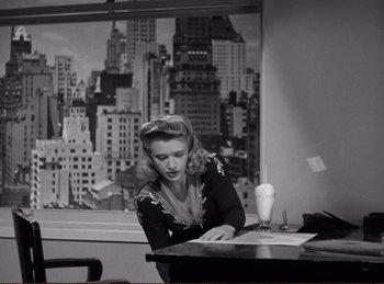 Movie still from “Saboteur” (1942), directed by Alfred Hitchcock – A woman sitting at a table with a drink in front of a window; Medium shot, High angle