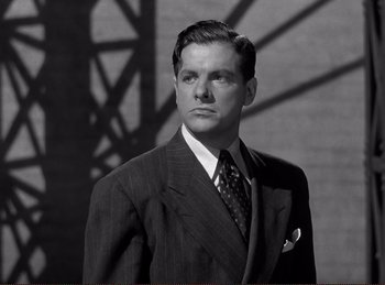 Movie still from “Saboteur” (1942), directed by Alfred Hitchcock – A man wearing a suit and tie standing in front of a wall; Close Up shot, Low angle