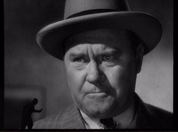 Movie still from “Saboteur” (1942), directed by Alfred Hitchcock – An old photo of a man in a suit and a hat; Close Up shot, Low angle