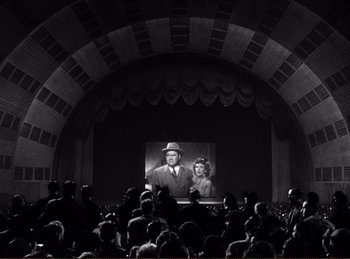 Movie still from “Saboteur” (1942), directed by Alfred Hitchcock – A crowd of people watching a movie on a screen; Extreme Wide shot, High angle