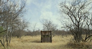 Movie still from “Safari” (2016), directed by Ulrich Seidl – An open field with trees and a wooden structure in the middle of it; Extreme Wide shot, Low angle