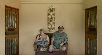 Movie still from “Safari” (2016), directed by Ulrich Seidl – An older man sitting next to an older woman on a couch; Medium shot, High angle