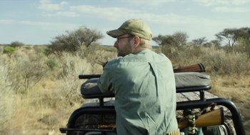Movie still from “Safari” (2016), directed by Ulrich Seidl – A man with a rifle in his hand and a hat on; Medium shot, Over the shoulder angle