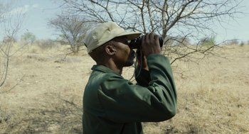 Movie still from “Safari” (2016), directed by Ulrich Seidl – A man looking through binoculars while standing in a field; Close Up shot, Over the shoulder angle