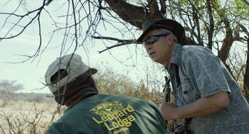 Movie still from “Safari” (2016), directed by Ulrich Seidl – A man in a cowboy hat talks to another man in a green shirt; Medium shot, Over the shoulder angle