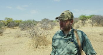 Movie still from “Safari” (2016), directed by Ulrich Seidl – A man wearing a hat standing in the desert; Medium shot, Over the shoulder angle