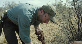 Movie still from “Safari” (2016), directed by Ulrich Seidl – A man in a hat and glasses working in a field; Medium shot, Low angle