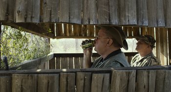 Movie still from “Safari” (2016), directed by Ulrich Seidl – A man in a hat drinking from a cup; Medium shot, Over the shoulder angle