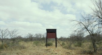Movie still from “Safari” (2016), directed by Ulrich Seidl – An outhouse in the middle of a dry grass field; Extreme Wide shot, Low angle