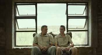 Movie still from “Safari” (2016), directed by Ulrich Seidl – A couple of men sitting next to each other on a couch; Medium shot, Low angle