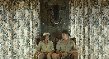 Movie still from “Safari” (2016), directed by Ulrich Seidl – A man and a woman sitting on a couch in front of an animal print wall; Wide shot, Low angle