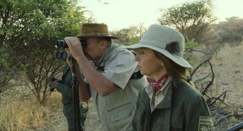 Movie still from “Safari” (2016), directed by Ulrich Seidl – A man and a woman in a field taking pictures with binoculars; Medium shot, Over the shoulder angle