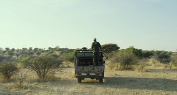 Movie still from “Safari” (2016), directed by Ulrich Seidl – A man riding on the back of a truck in the desert; Wide shot, Low angle