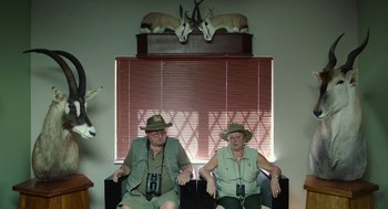 Movie still from “Safari” (2016), directed by Ulrich Seidl – A couple of men sitting next to each other on a couch; Medium shot, High angle
