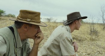 Movie still from “Safari” (2016), directed by Ulrich Seidl – Two men sitting in a field with hats on their heads; Close Up shot, Over the shoulder angle