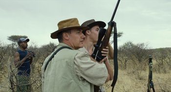 Movie still from “Safari” (2016), directed by Ulrich Seidl – A man and a man holding a rifle in a field; Medium shot, Low angle