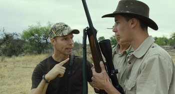 Movie still from “Safari” (2016), directed by Ulrich Seidl – A man holding a rifle and pointing at another man holding a gun; Medium shot, Over the shoulder angle